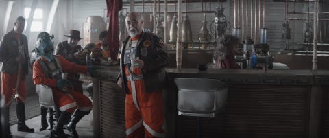 new republic pilots including trapper wolf dave filoni, wearing hat, captain carson teva paul sun hyung lee, in center with bartender misty rojas in a scene from lucasfilm's the mandalorian, season three, exclusively on disney ©2023 lucasfilm ltd tm all rights reserved