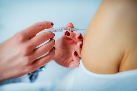 Female Doctor Injecting Syringe On Woman Shoulder In Hospital