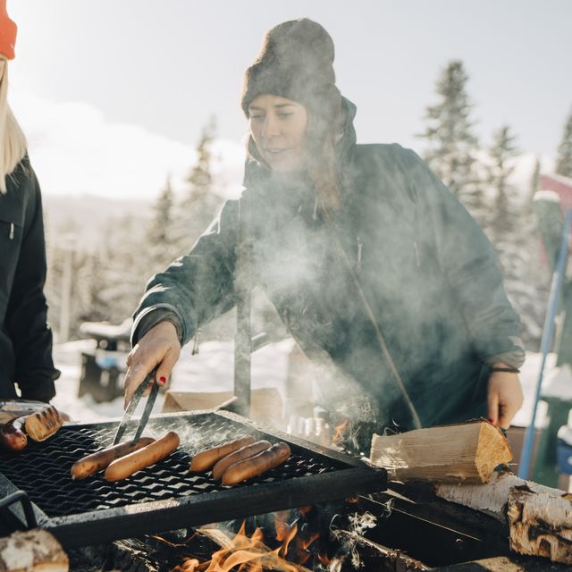 female friends preparing sausages on barbecue grill during winter