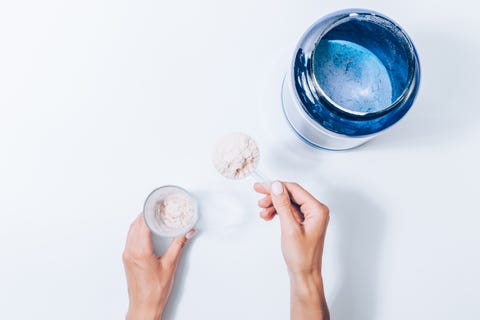 Main féminine tenant une cuillère avec de la poudre de compléments sportifs