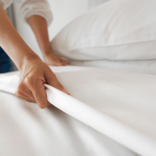 female hand set up white bed sheet in bedroom