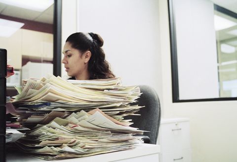 female office worker sitting at desk with pile of paperwork