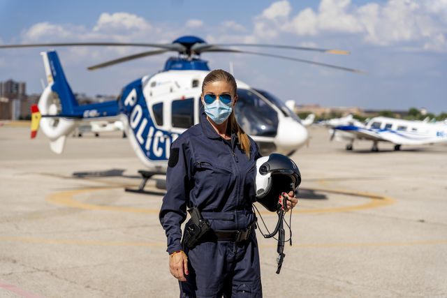 female police pilot wearing protective face mask while standing against helicopter