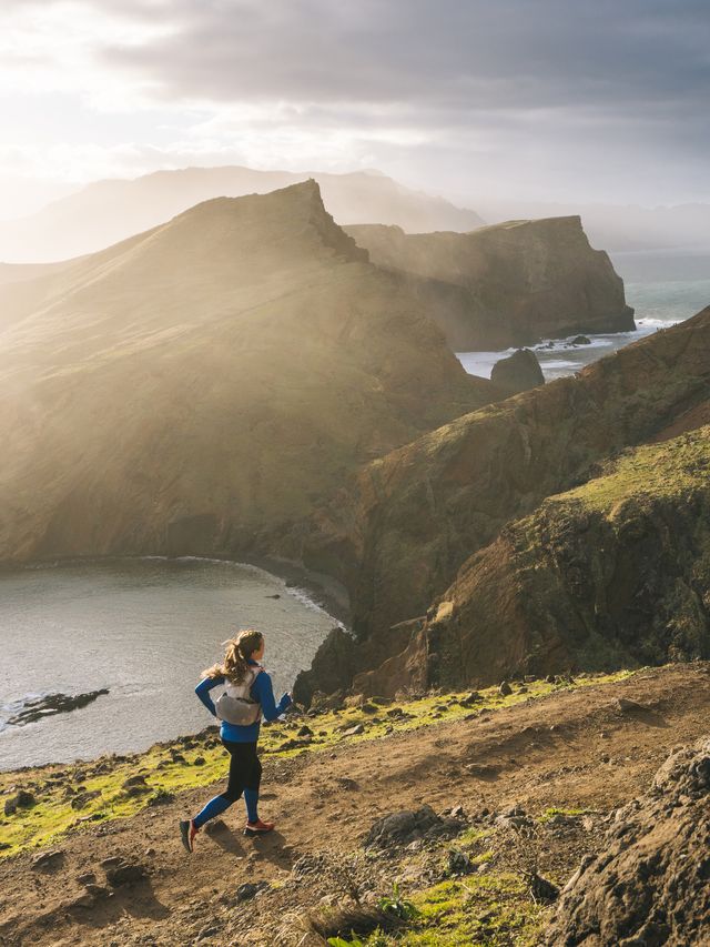 female trail runner traverses trail above coastline, cliffs