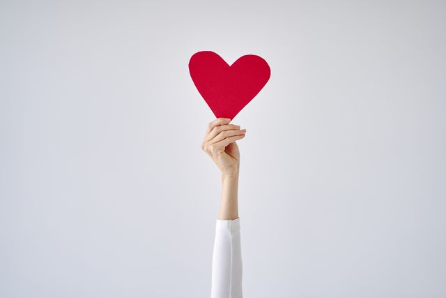 females hand holding red heart against white grey background