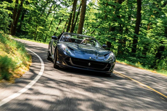 a black sports car driving down a road surrounded by trees