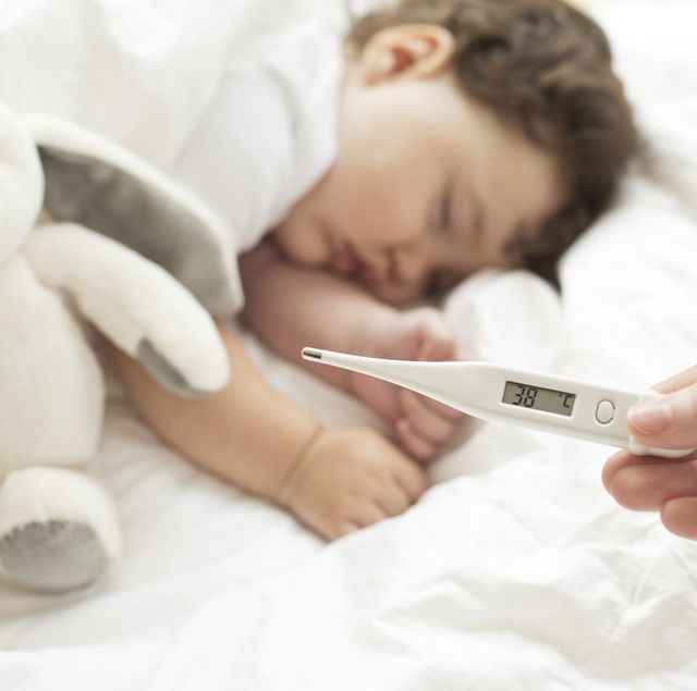 bebé dormido con fiebre, ta y como muestra el termómetro que hay frente al niño