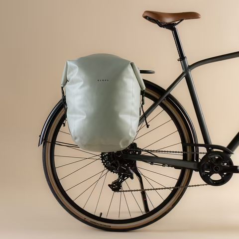 lichtgroene grijze fietstas aan een kant van de bagagedrager van een donkergrijze fiets met een lichtbruine achtergrond