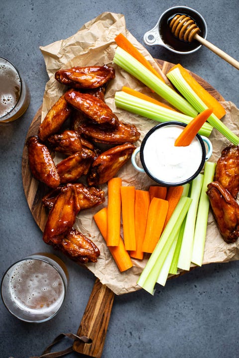 crispy baked honey chipotle wings with carrots and celery on wood board with beer