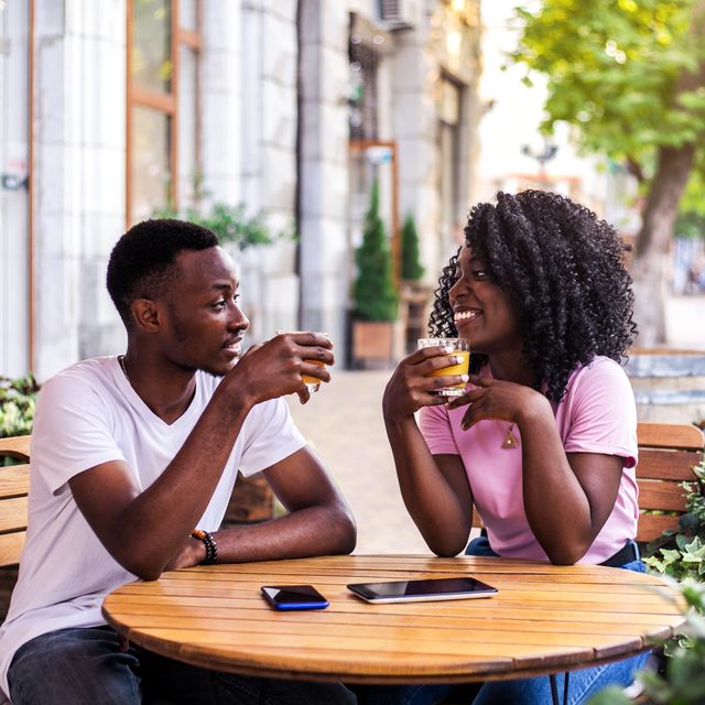 portrait of stylish black couple talking to each other at summer street cafe