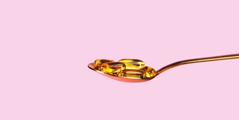 fish oil capsules with omega 3, vitamin d in a spoon on pink background