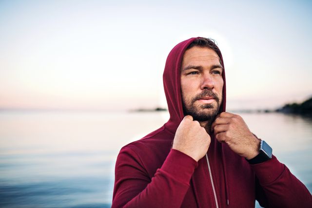 a fit mature sportsman runner standing outdoors on beach, hood on head copy space