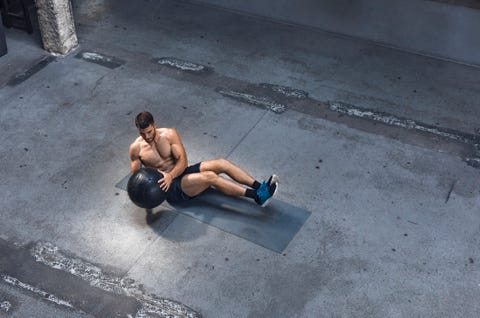 Mettre en place un jeune homme faisant de l'exercice à l'intérieur - Faire des exercices d'abdominaux avec un médecine-ball Mettre en place un jeune homme faisant de l'exercice à l'intérieur faisant des exercices abdominaux avec un médecine-ball