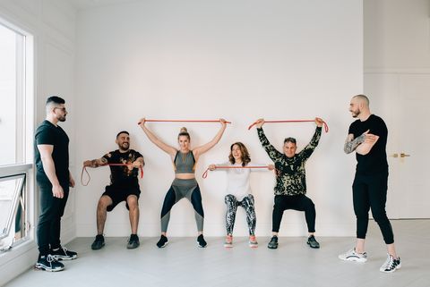 fitness instructors observing friends doing squat against wall with resistance band in studio