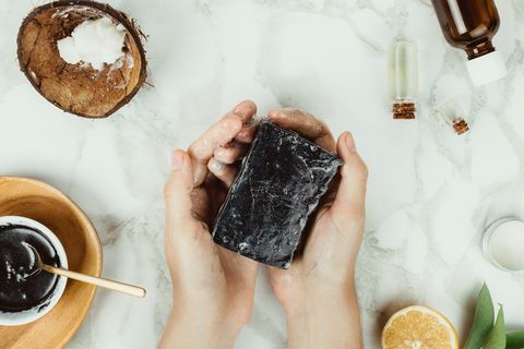 flatlay of woman's hands holding homemade charcoal soap with its ingredients on the side