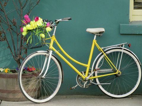 Flowers In Basket Of Yellow Bicycle Leaning On Wall