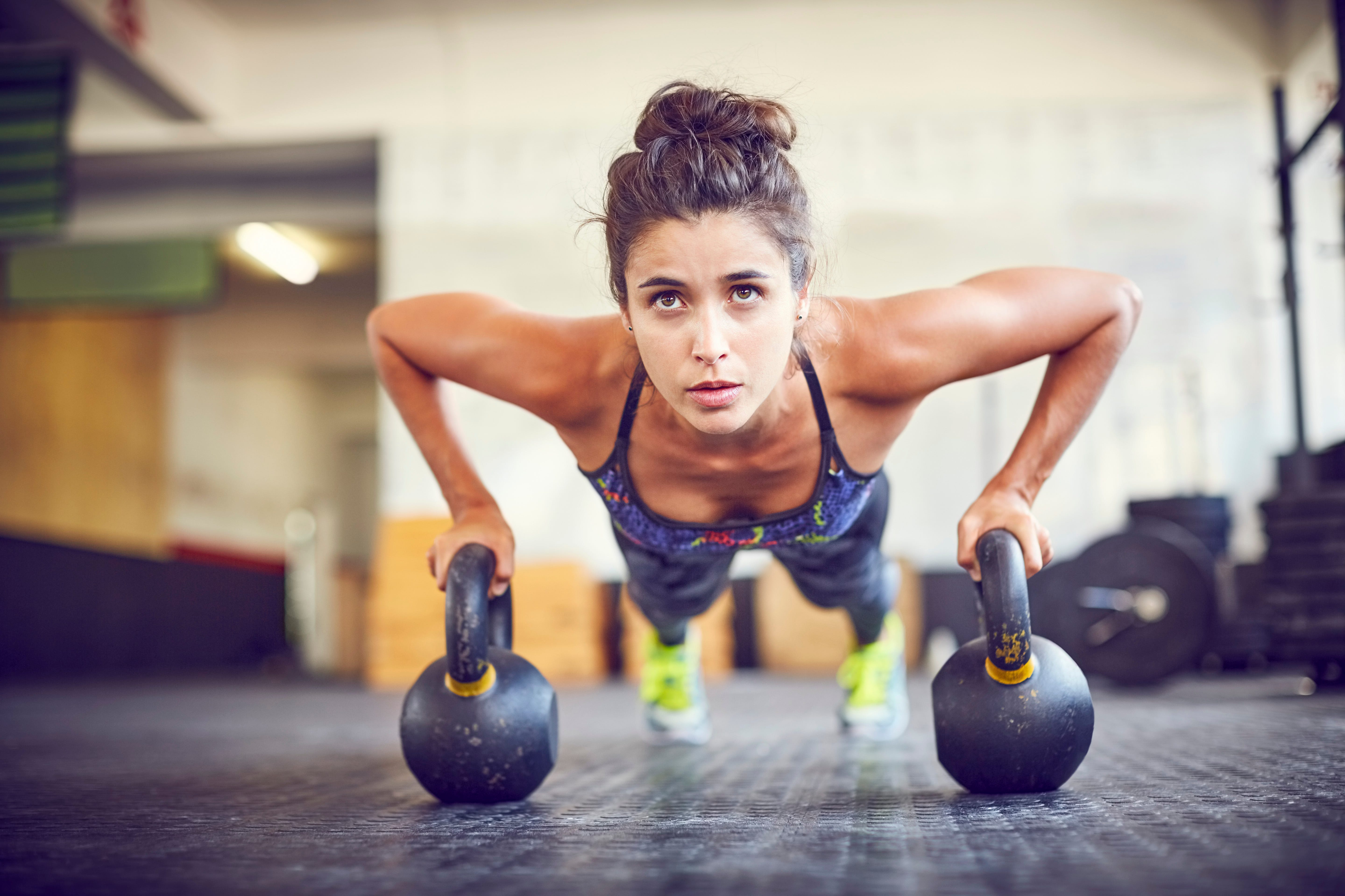 Atleta enfocado haciendo flexiones en pesas rusas en el gimnasio