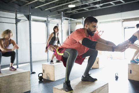 Focused man jump squats in gym exercise class