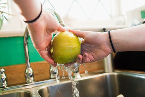 Washing green apple under running water in sink.