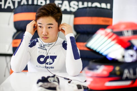 Yuki tsunoda helyezi a rádió fülhallgató, ahogy készül vezetni a Forma-1-es csapat scuderia alphatauri az ő bukósisak és tűzálló kesztyű az asztalon előtte, és halom gumiabroncsok takaró mögötte