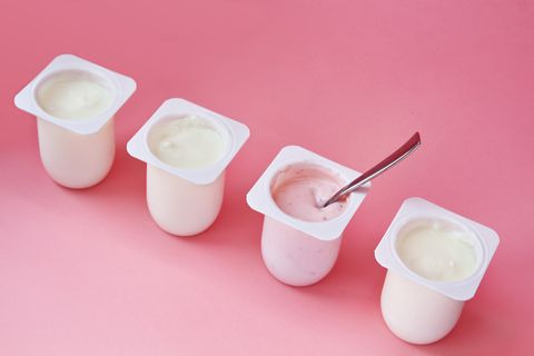 Four yogurts in white plastic cups on pink background in minimal style.