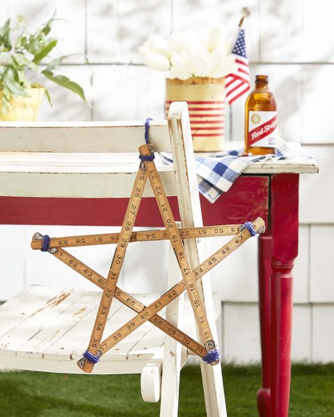 star shape made from a hinged carpenters ruler hung off the back of a rustic white wood folding chair for the 4th of july