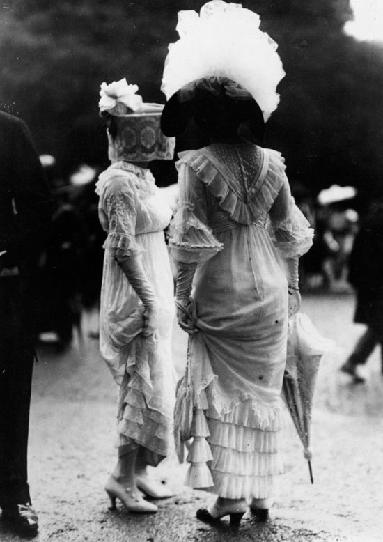 due donne del ventesimo secolo scattate da dietro con vestiti bianchi e ombrellini