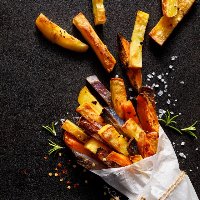 french fries,  baked fries from different types and colors of potatoes sprinkled with herbs and spices in paper bag on a black background