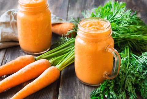 Fresh carrot smoothie in glass jars on rustic wooden background