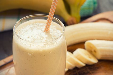 Fresh-made glass of banana smoothie with straw on wood