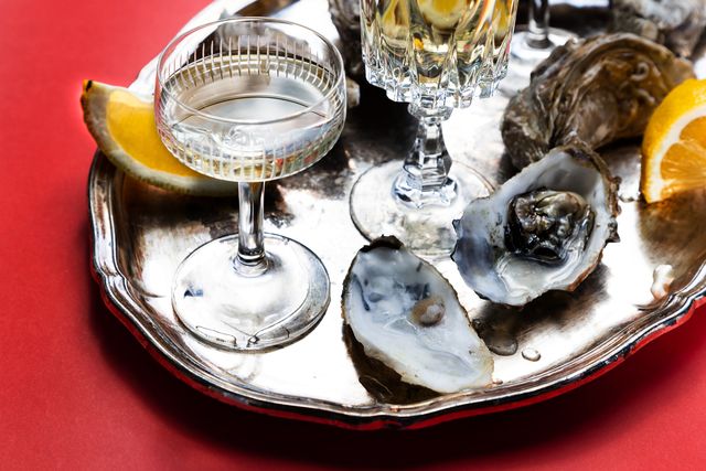 fresh oysters on a tray with lemon and white wine on a red background