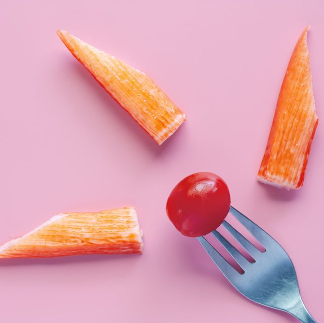 Fresh red tomato on fork with crab stick on pink background for food and eating concept