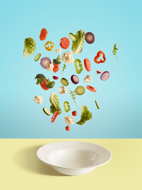 Fresh sliced vegetables and salad leaf falling into bowl