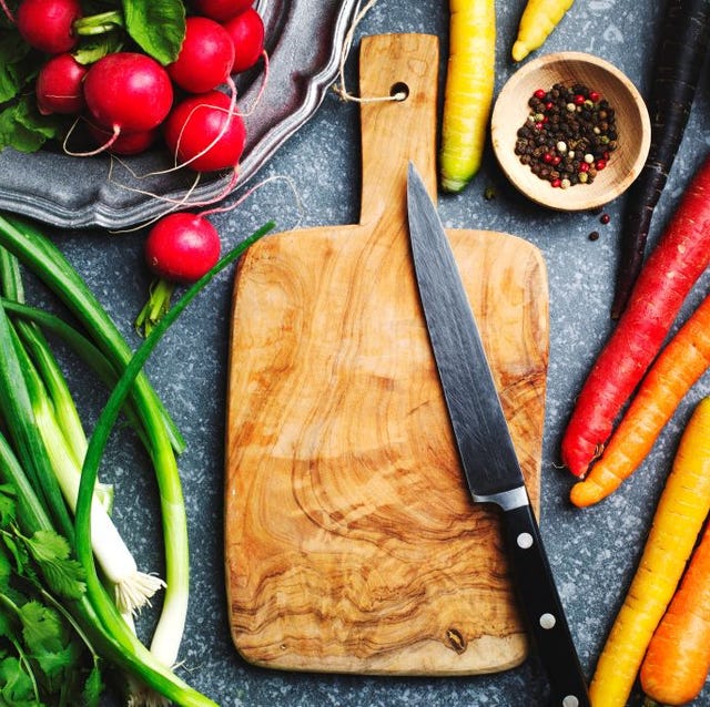Fresh spring vegetables around wooden cutting board with kitchen knife for vegetarian cooking, top view fresh spring vegetables around wooden cutting board with kitchen knife for vegetarian cooking, top view