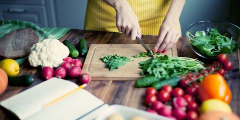 Mujer cortando verduras en una mesa con otros alimentos