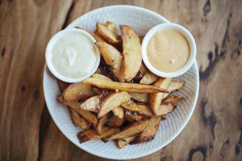 Gourmet potato wedges served with black sea salt & aioli in a white bowl, shot directly above