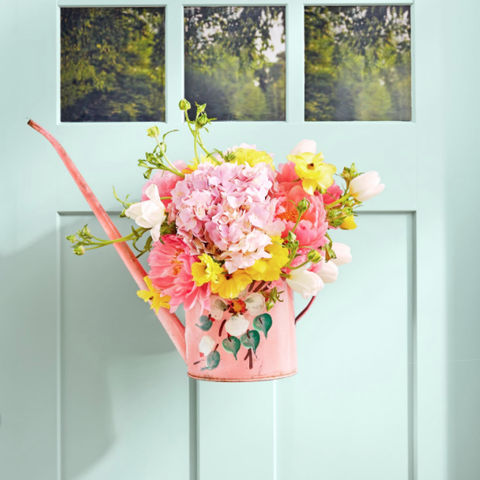 arrangement of flowers in a pink watering can hanging on a front door