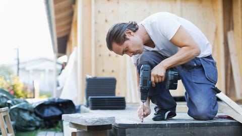 Full length of man using cordless screwdriver nail into floorboard Full length of man using cordless screwdriver nail into floorboard