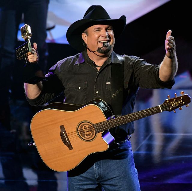 country star garth brooks performing with a guitar wearing a black cowboy hat and black button down shirt