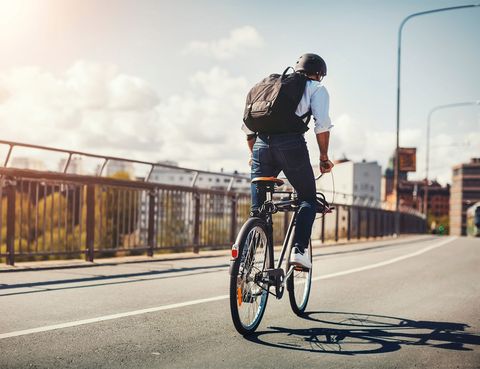 rear view of businessman riding bicycle on bridge in city