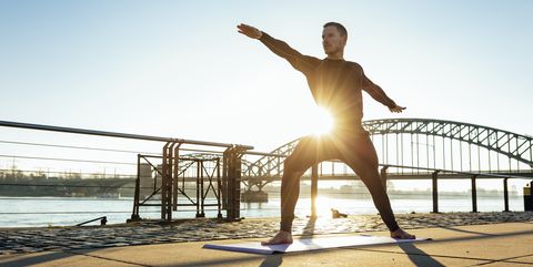 Germany, Cologne, Young man practicing yoga at the riverside