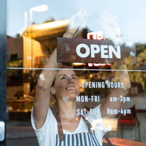 portrait of a happy business owner hanging an open sign on the door at a cafe and smiling   food and drinks concepts