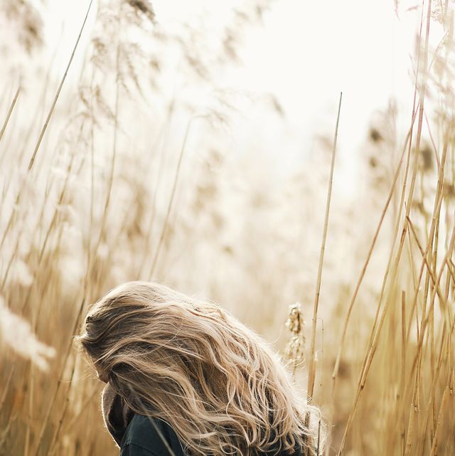 Rear View Of Woman With Blond Hair Standing Amidst Dry Plants On Field