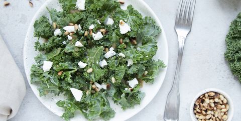 fresh kale salad with goat cheese, pine nuts and sweet balsamic vinegar dressing with onion on grey background