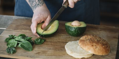 Vrouw snijdt avocado naast hamburgerbroodje 