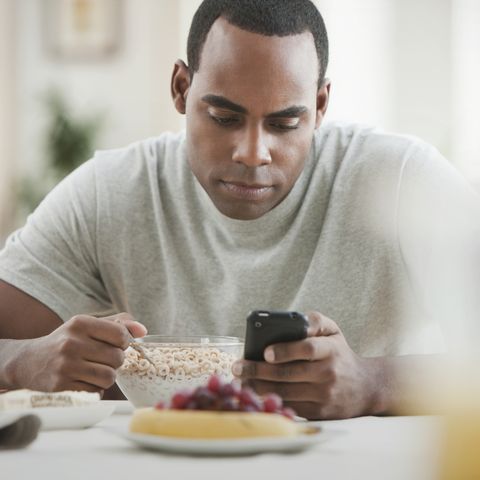 man text messaging and eating breakfast hungry men's health