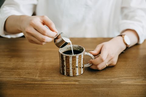 Close up shot of woman pouring milk in coffee cup and ready to enjoy it
