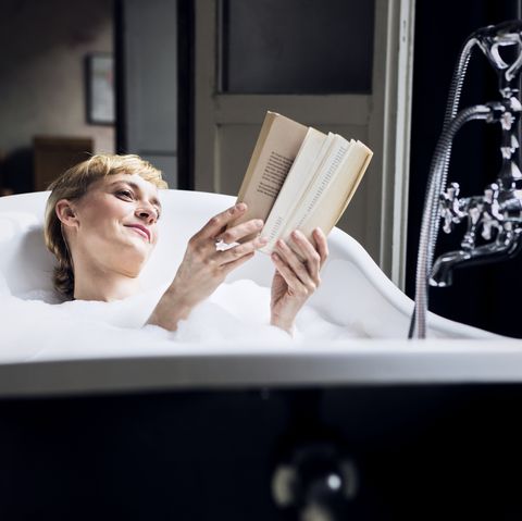 Portrait of relaxed woman taking bubble bath in a loft reading a book
