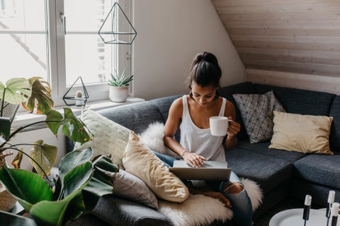 young woman sitting on the couch with cup of coffee using laptop