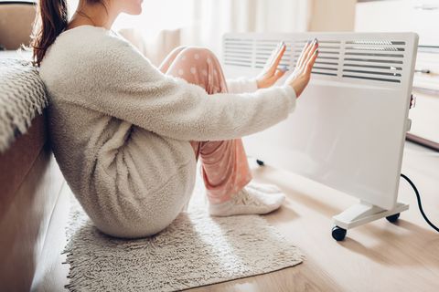 using heater at home in winter woman warming her hands sitting by device and wearing warm clothes heating season